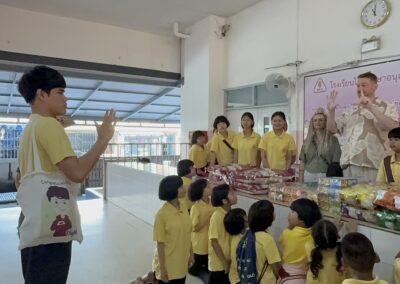 Kinder mit Snacks posieren mit vier Erwachsenen vor einem Holzpavillon, viele zeigen das Liebe-Zeichen.